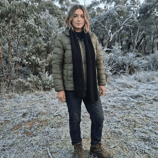 Person wearing a green puffer jacket and black scarf standing in a frosty forest.