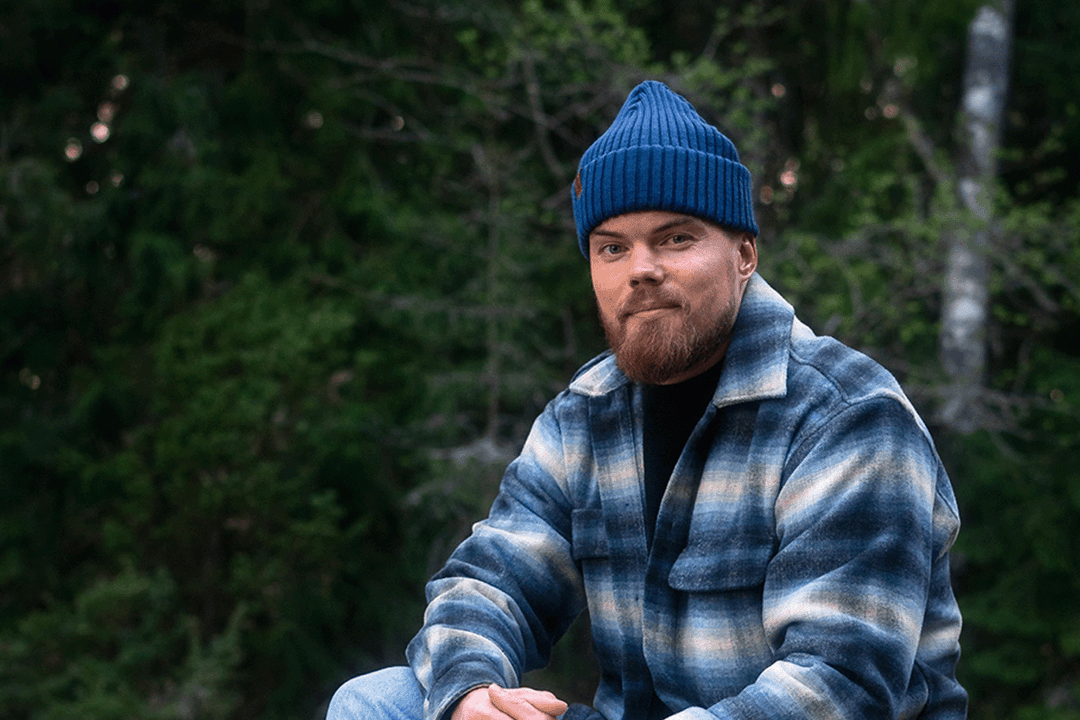 Man wearing a blue beanie and plaid jacket sitting in a forest