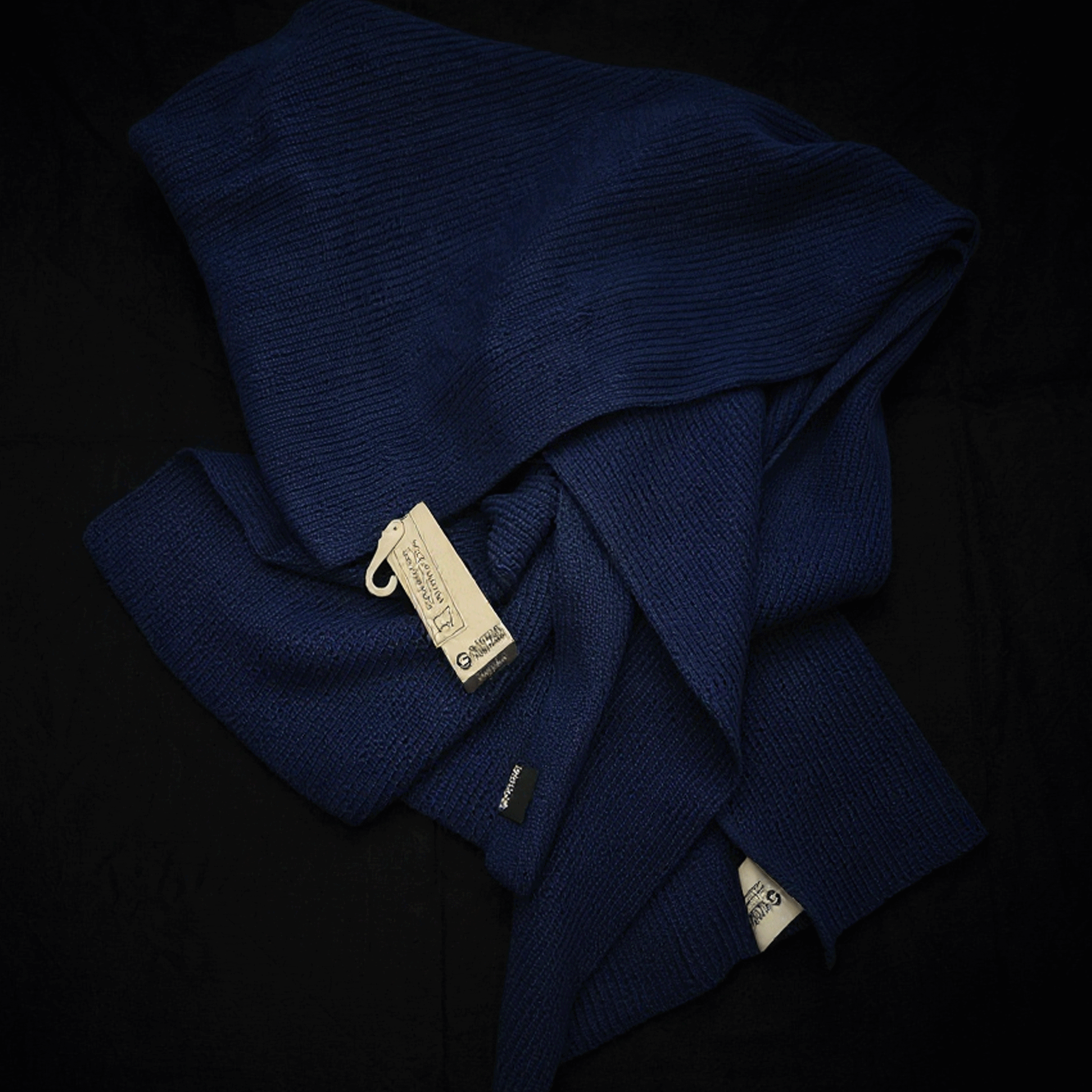 Folded navy blue scarf with a brand tag on a black background