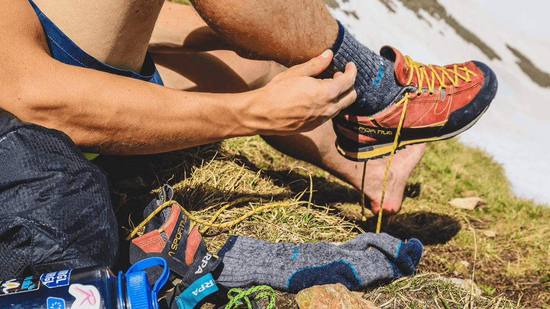 Person tying shoelaces on hiking shoes with outdoor socks on the ground